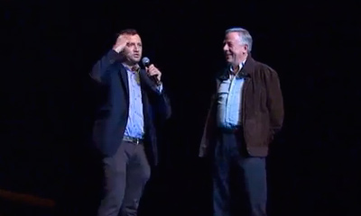 two men talking on a darkened stage